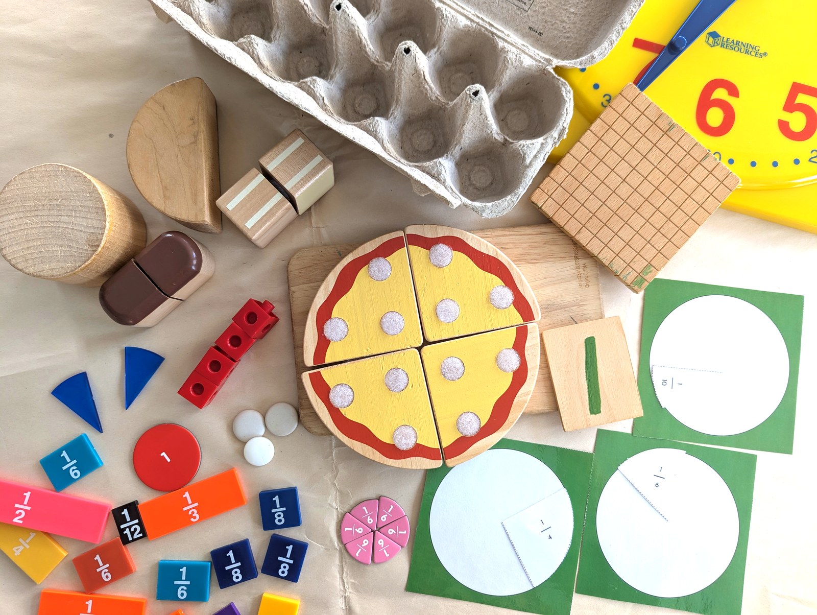 Classroom math manipulatives — fraction tiles, wooden pizza, base-10 blocks, and more — laid out on a table